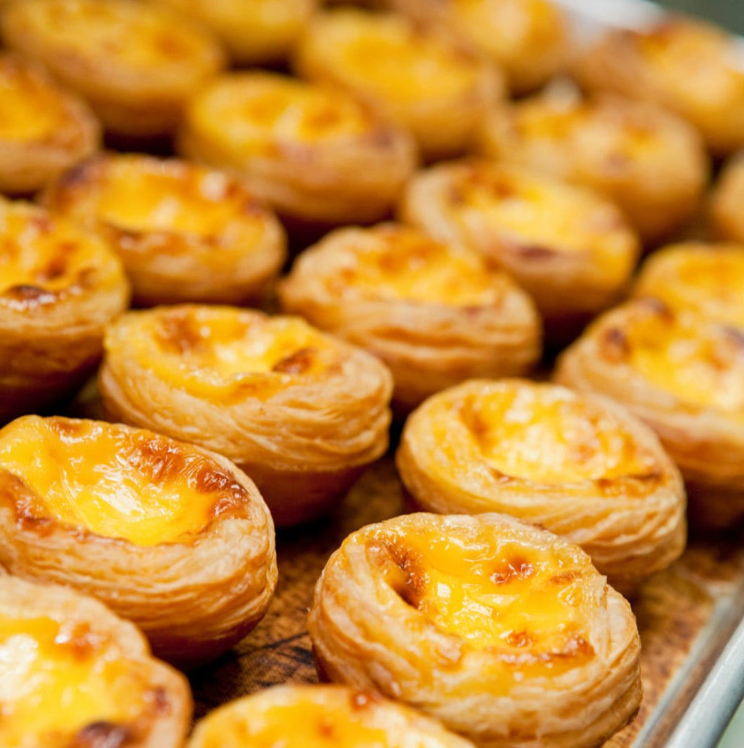 Golden baked egg tarts with flaky puff pastry shells and creamy custard filling, arranged on a baking tray.